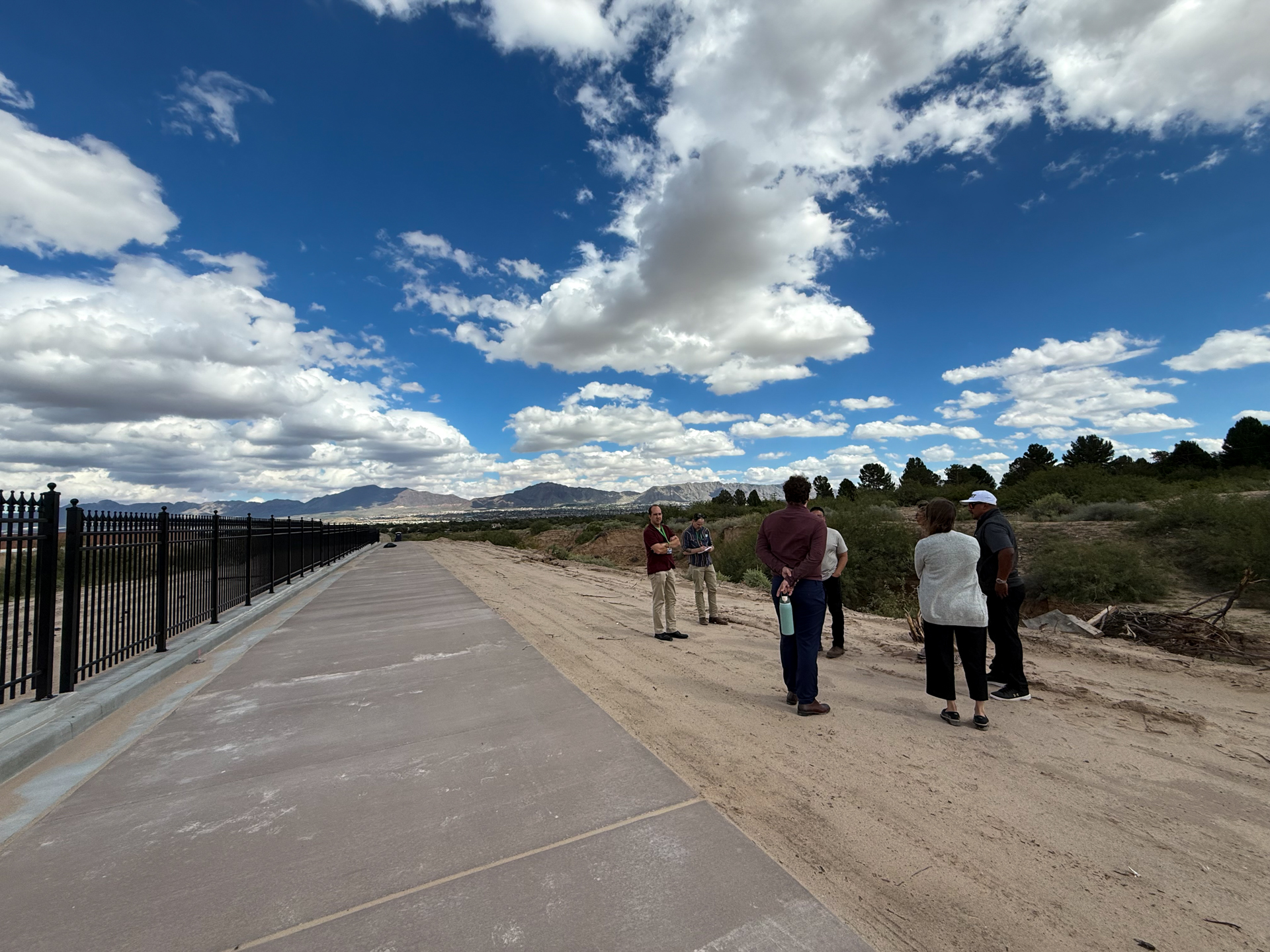A paved walking path alongside a black iron fence with mountain views