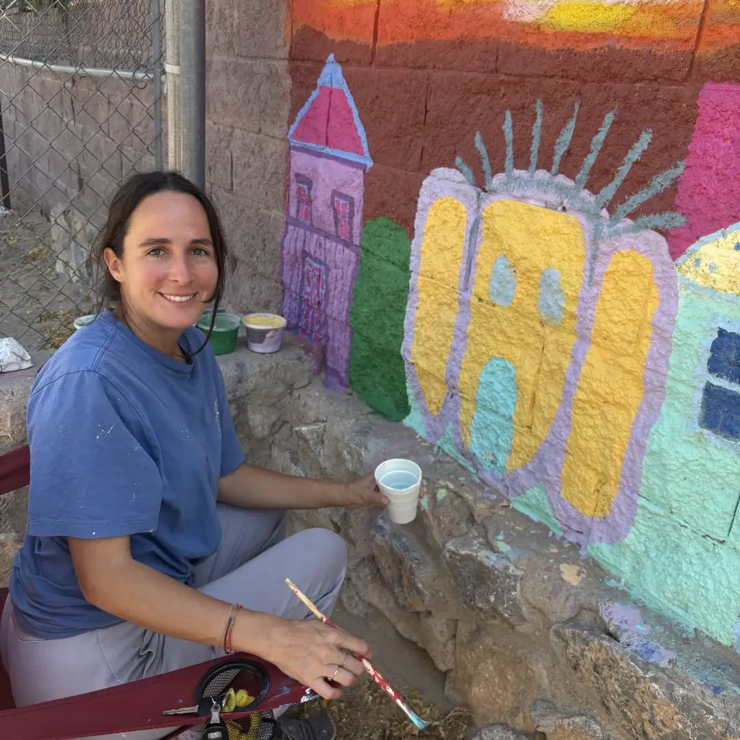 A smiling volunteer sits by the wall with a paintbrush.