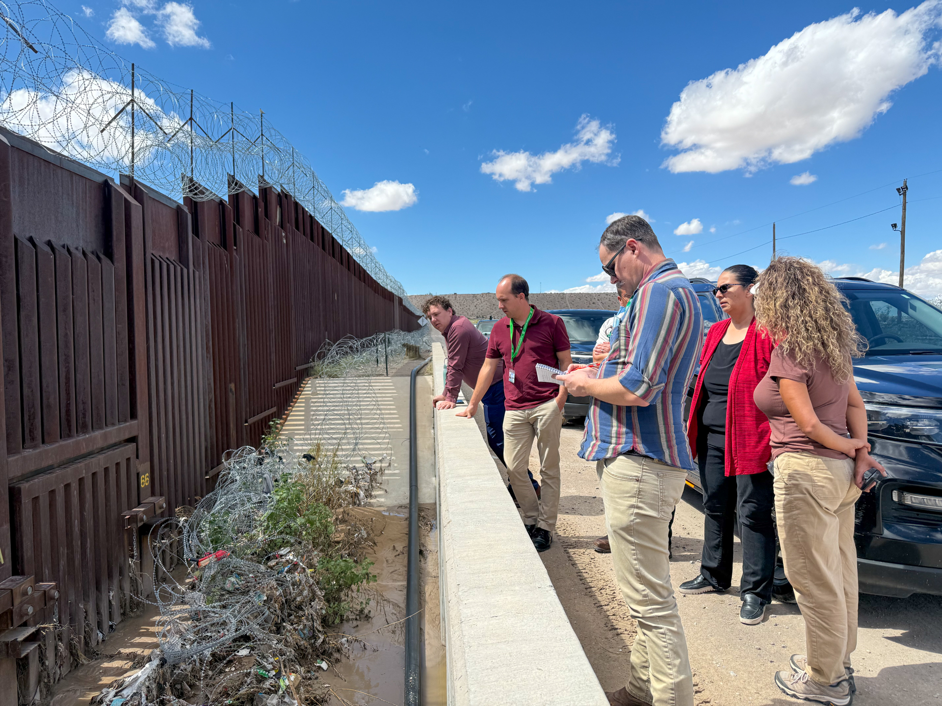 Tour participants looking down at a drainage channel next to the border wall
