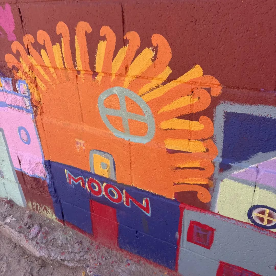 Detail of a painted orange casita under a bright sun, with the word Moon on the wall.