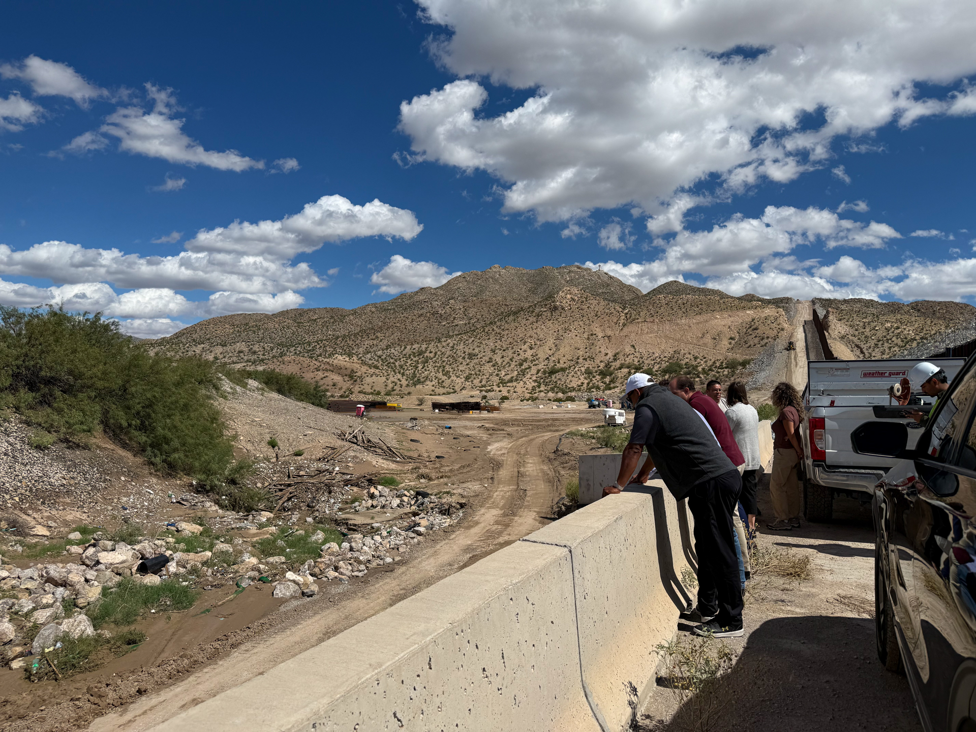 Participants observing drainage conditions with hills and equipment in the background