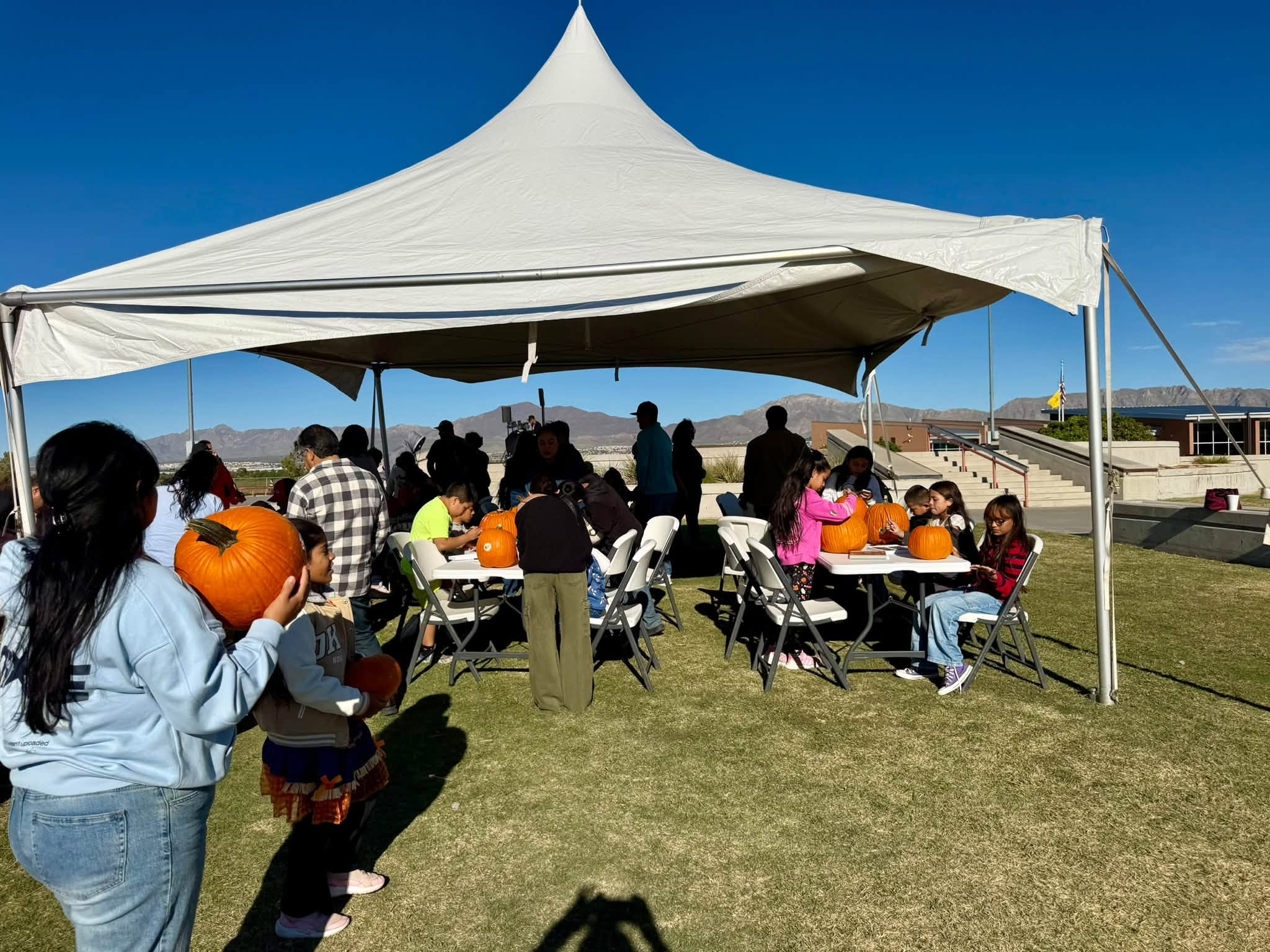 Children paint pumpkins at tables under a large white tent