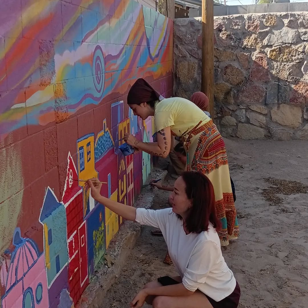 Two volunteers painting colorful casitas on the mural wall.